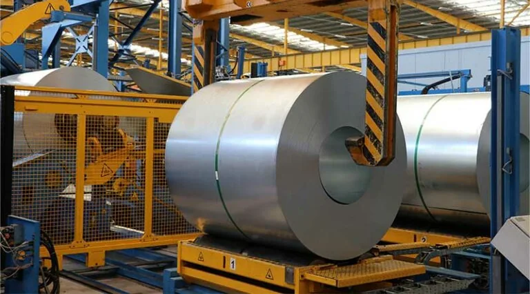 A steel coil on a transfer car at a coil change, with the changeover crane's hook beside it and more coils waiting behind.